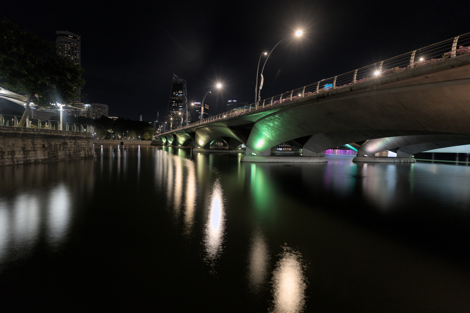 A bridge across the water of the Singapore river. The water is glassy from the longer exposure time.
